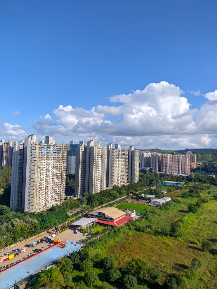 hero-img-02 Aerial view of tall residential buildings in Pune, India, with lush greenery and a vibrant sky.